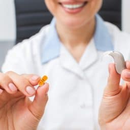 Audiologist holding a hearing aid and battery.