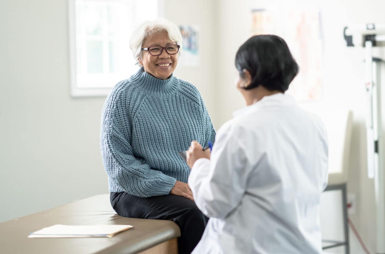 Older woman sitting on the exam table and talking with her primary care provider.