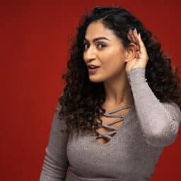 Young woman holding her hand to her ear, hearing concept