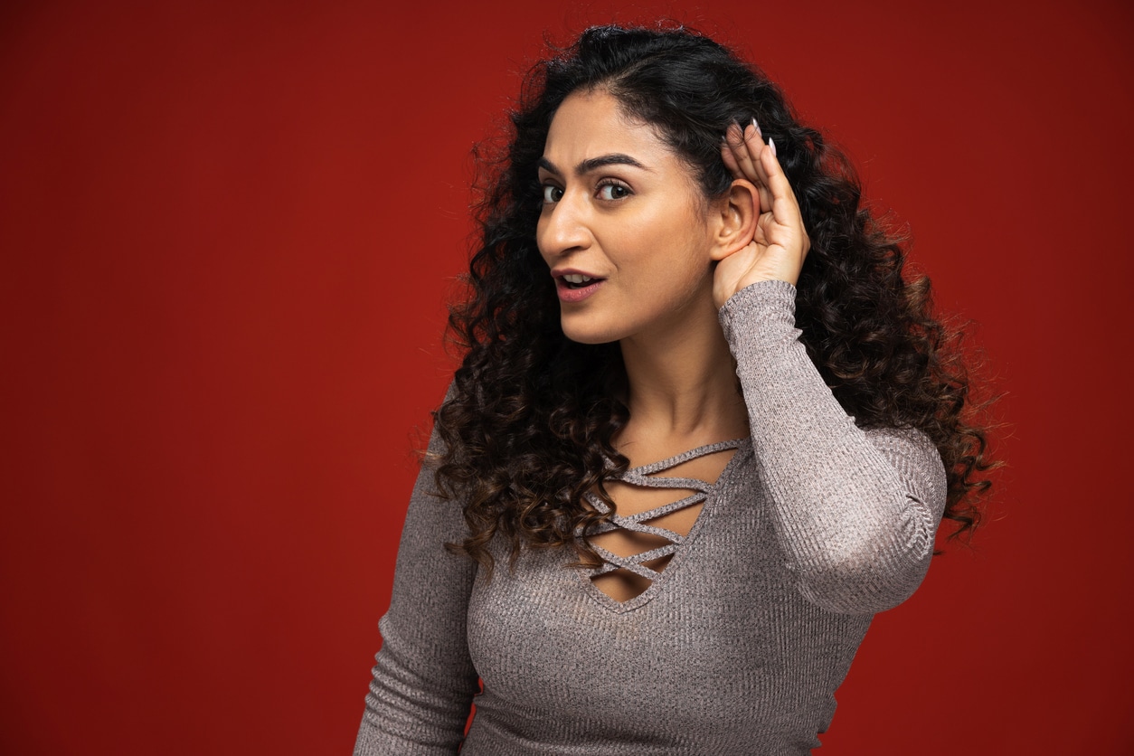 Young woman holding her hand to her ear, hearing concept.