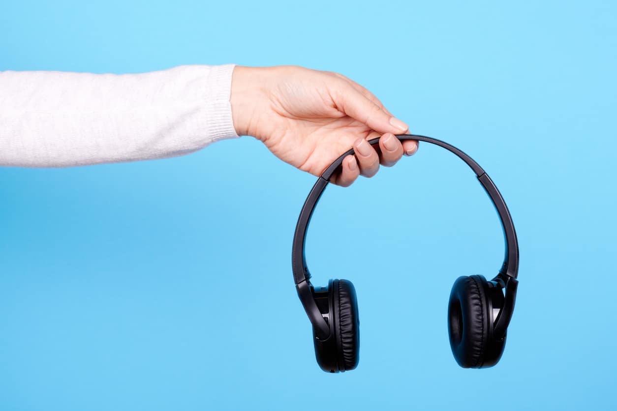 Hand with black wireless headphones on blue background.