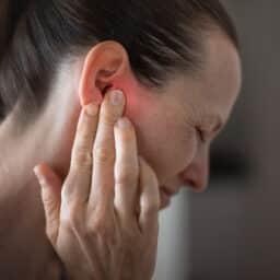 Woman holding her red ear and grimacing.