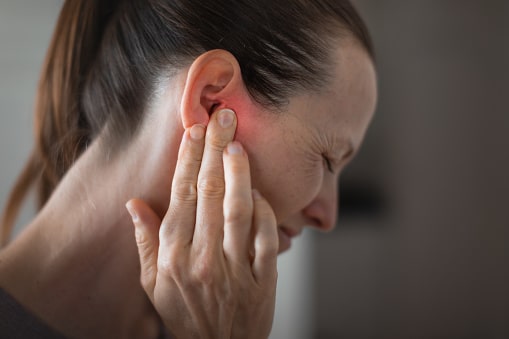 Woman holding her red ear and grimacing. 