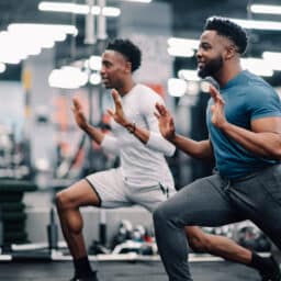 Two young men doing lunges in the gym.