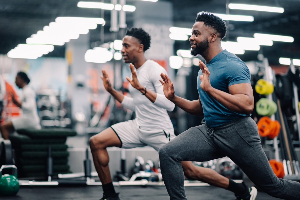 Two young men doing lunges in the gym.
