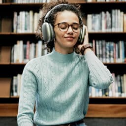 Happy woman, headphones and listening with audio book in library.